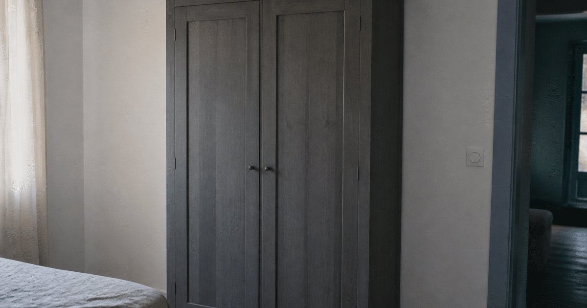 Armoire bois gris debout contre mur blanc avec portes fermees