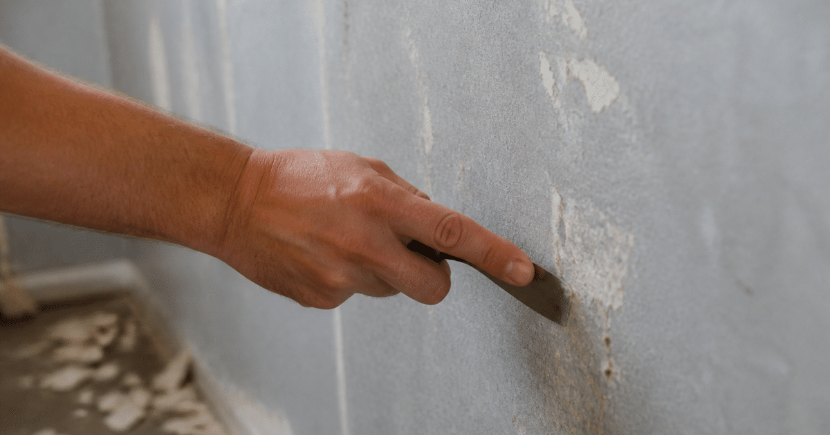 Main grattant doucement residus adhesifs sur papier peint gris